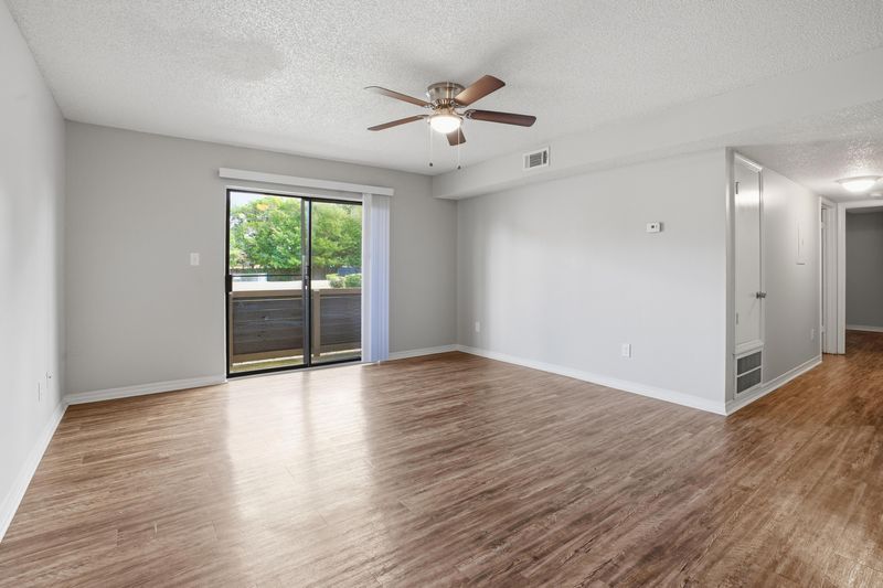 Empty apartment interior with hardwood floors, white walls, and natural lighting from windows.