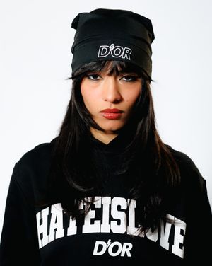 Stylish model wearing a black D'or beanie and Hatteisgate streetwear hoodie against white background.