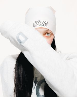Person wearing white cap with D'or logo against white background in artistic portrait style composition.