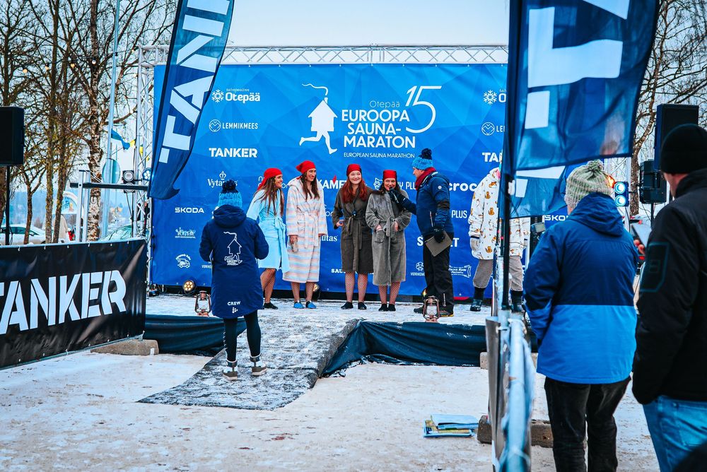 Event staff in blue uniforms setting up branded banners and displays at an outdoor winter sports competition area.