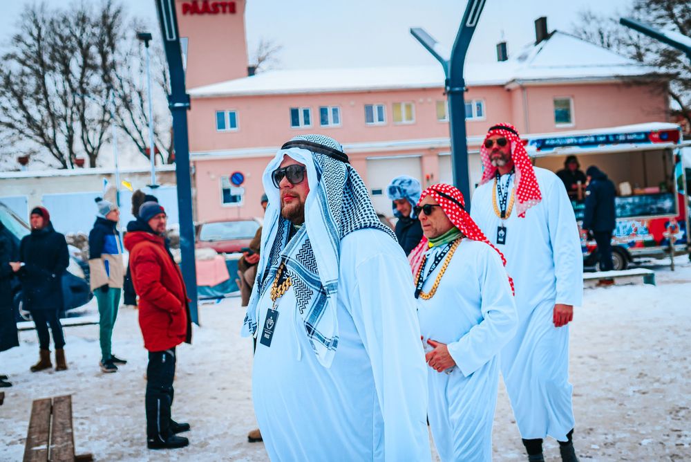 Winter scene showing people in white protective suits and red accents playing in snowy outdoor area.