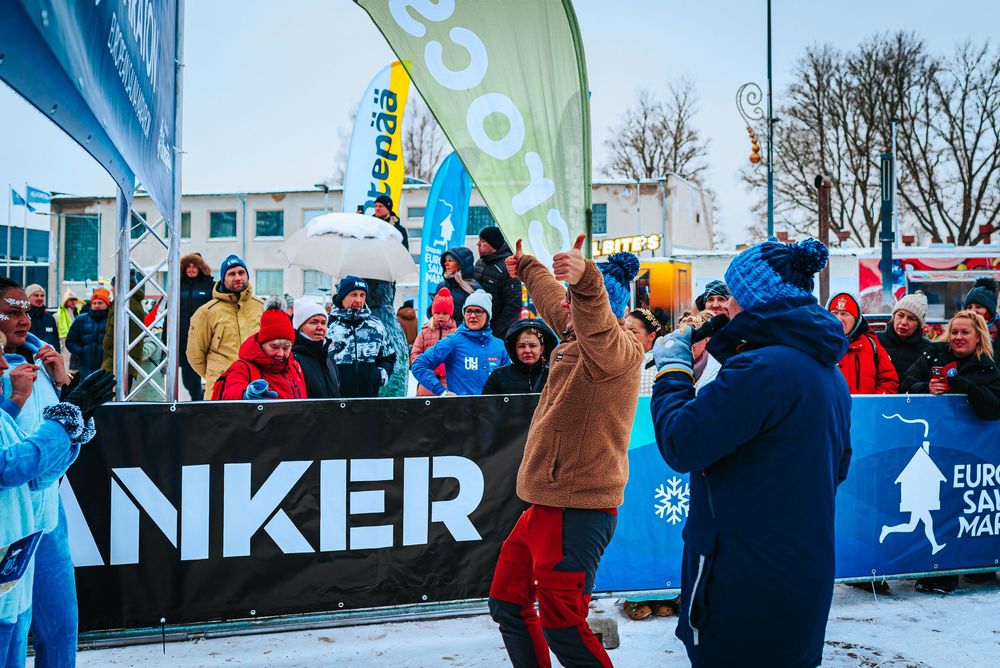 Runners participate in a winter marathon event with colorful banners and spectators lining the snowy course.