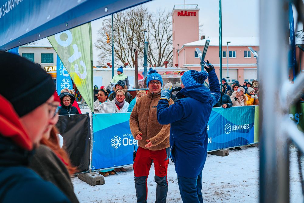 Spectators gather outside in winter to watch a competitive event in snowy conditions with blue barriers visible.