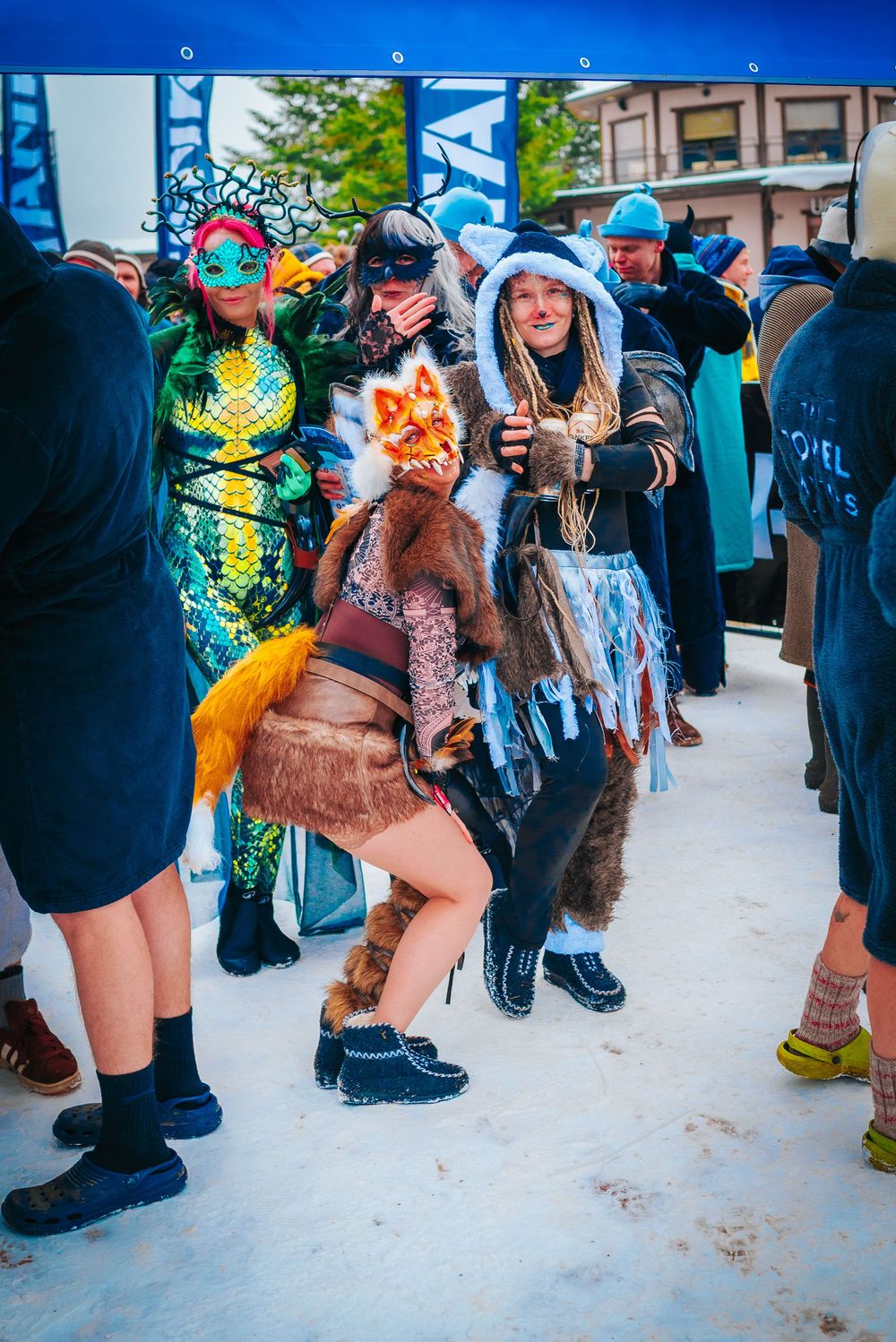 People in colorful costumes and outfits stand in snowy conditions during an outdoor winter event.