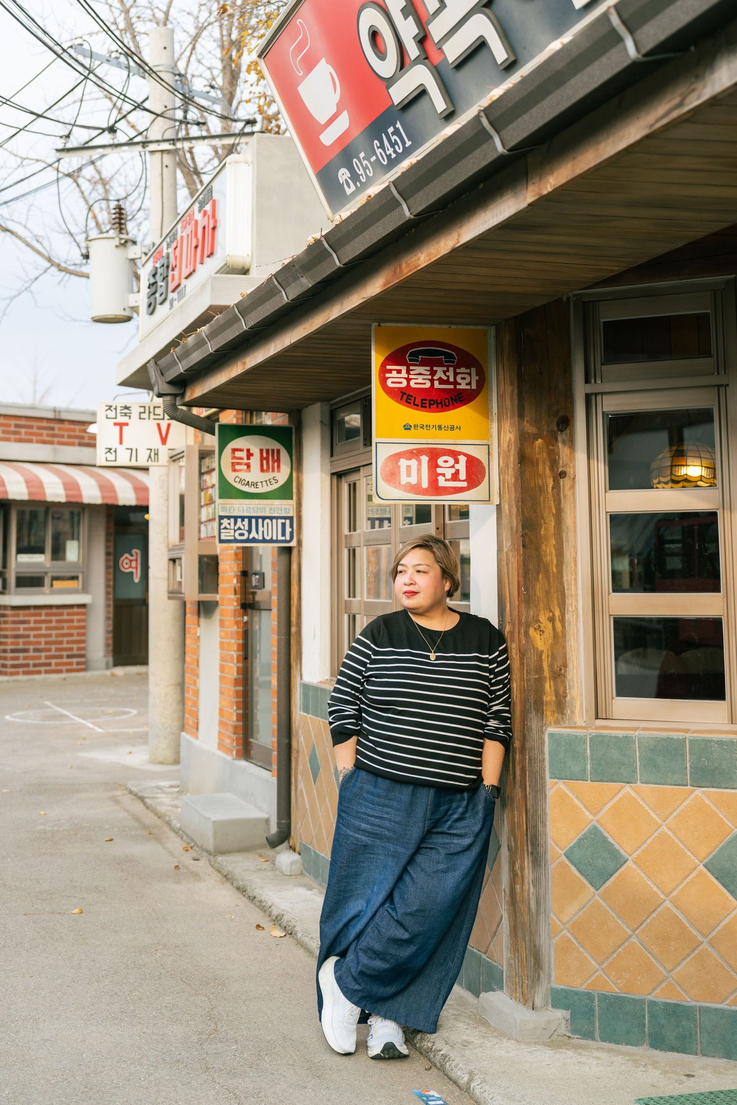 A series of connected images showing a person in a striped shirt and blue skirt standing near Korean storefronts.