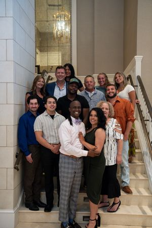 A group of people pose together on marble steps in formal attire at an event.