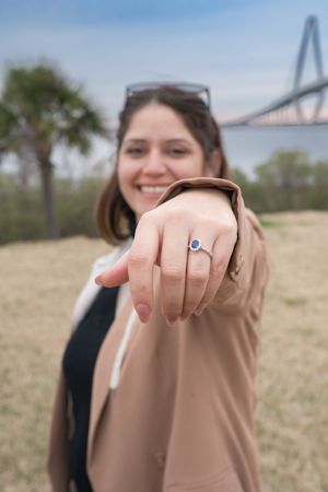 A close-up shot of a hand showing off an engagement ring with a bridge visible in the background.
