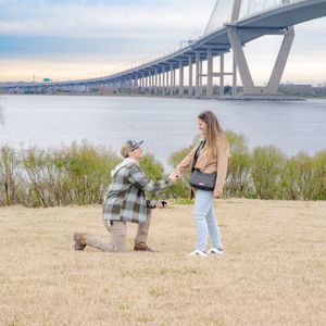 Couple shares tender moment on grassy hill overlooking Charleston's Ravenel Bridge at sunset.