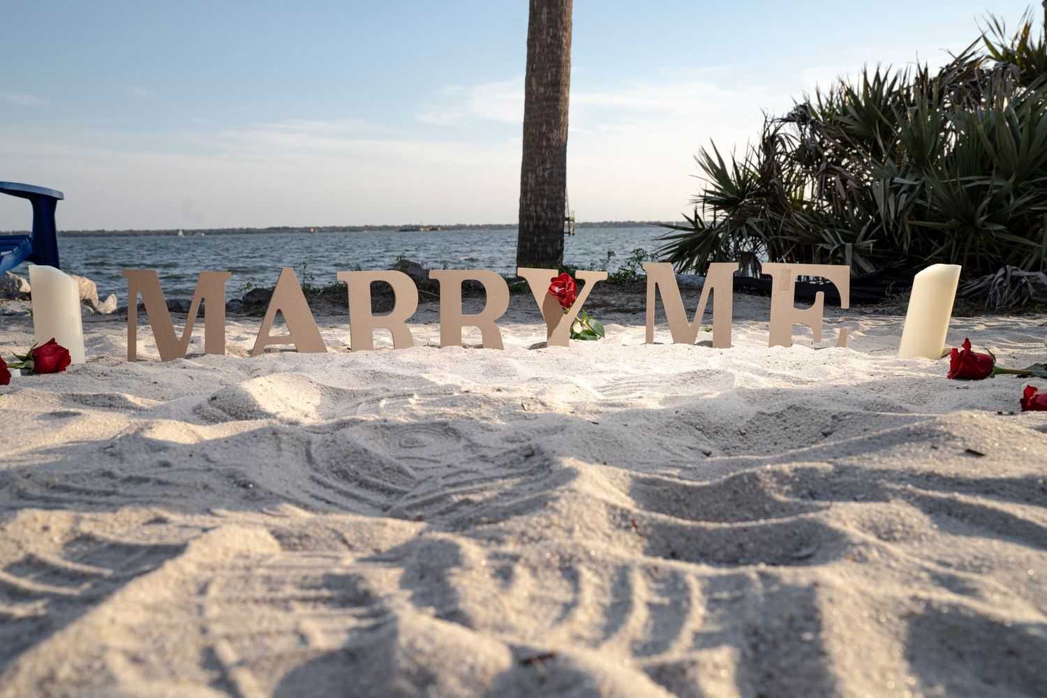 Colorful beach towels laid out on pristine white sand with palm trees and ocean waves in the background.