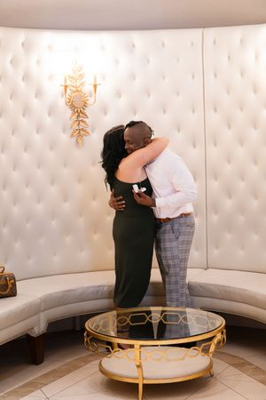 Couple embraces while dancing in an elegant white lounge area with curved seating and gold accents.