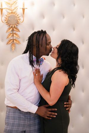 A romantic couple embraces intimately against an elegant white tufted backdrop.