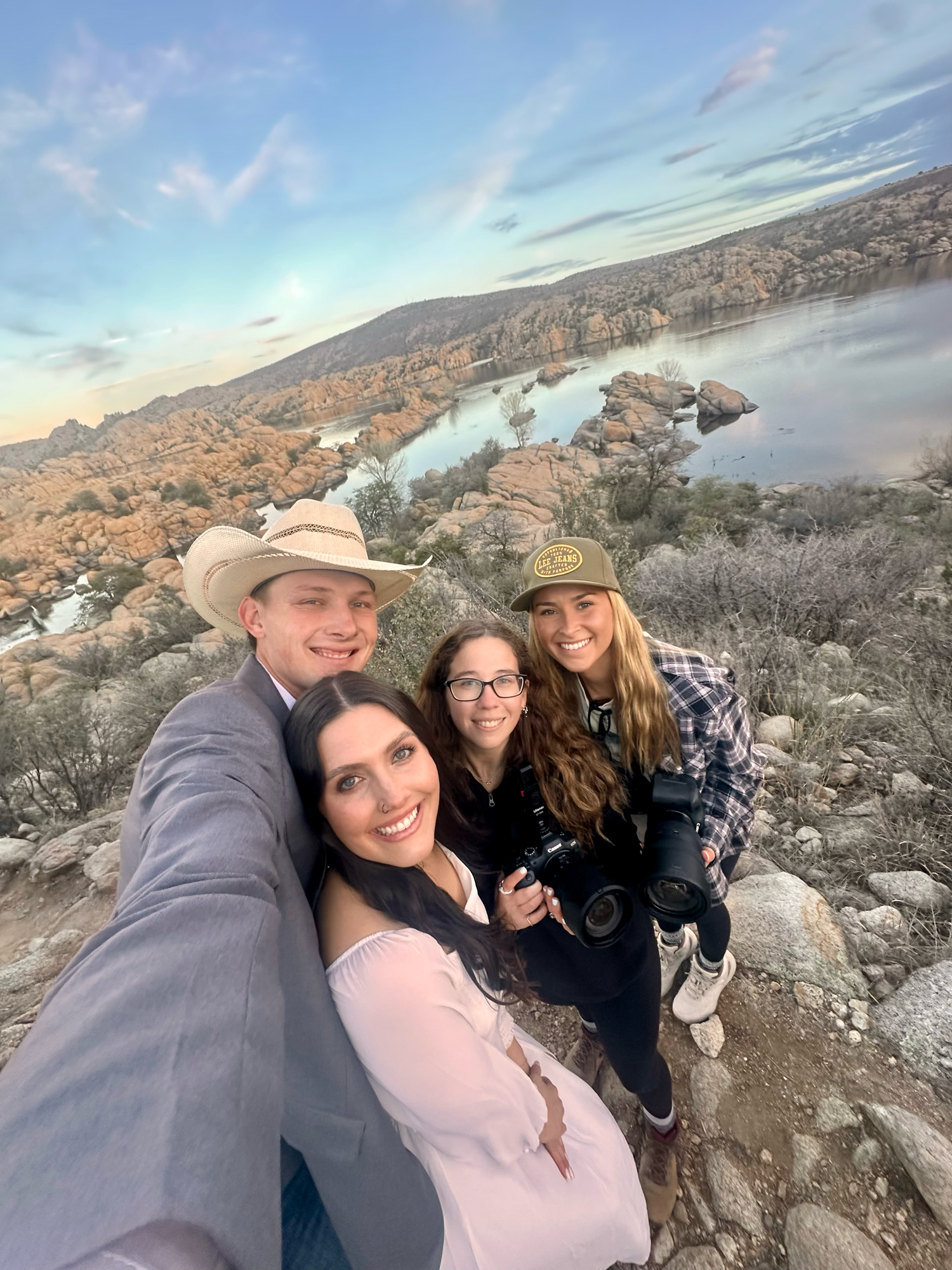 Group of friends taking selfies together against a scenic desert mountain landscape during golden hour.