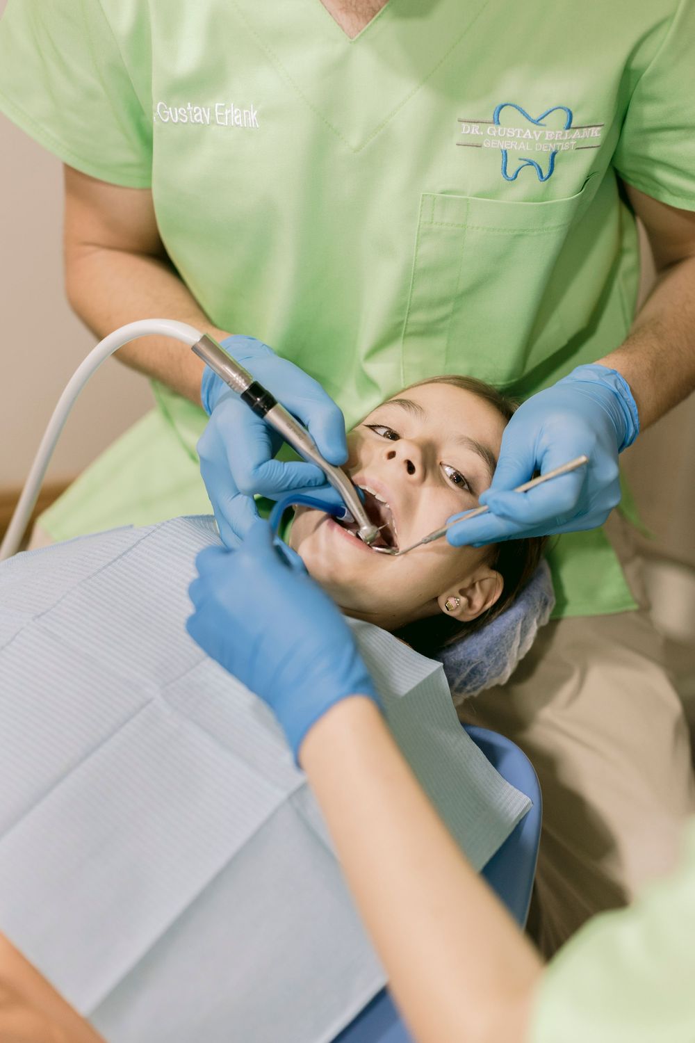 Two dentists in green scrubs and blue gloves performing a dental procedure on a patient in a dental chair.
