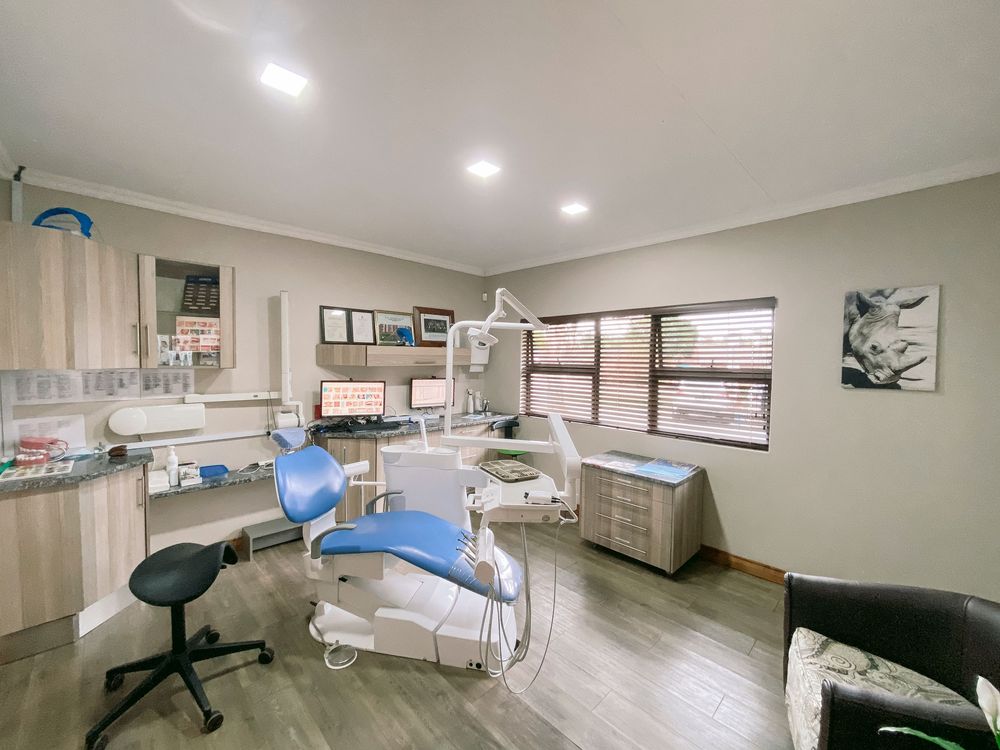 Modern dental operatory room with blue patient chair, dental equipment, wood flooring, and built-in cabinetry.