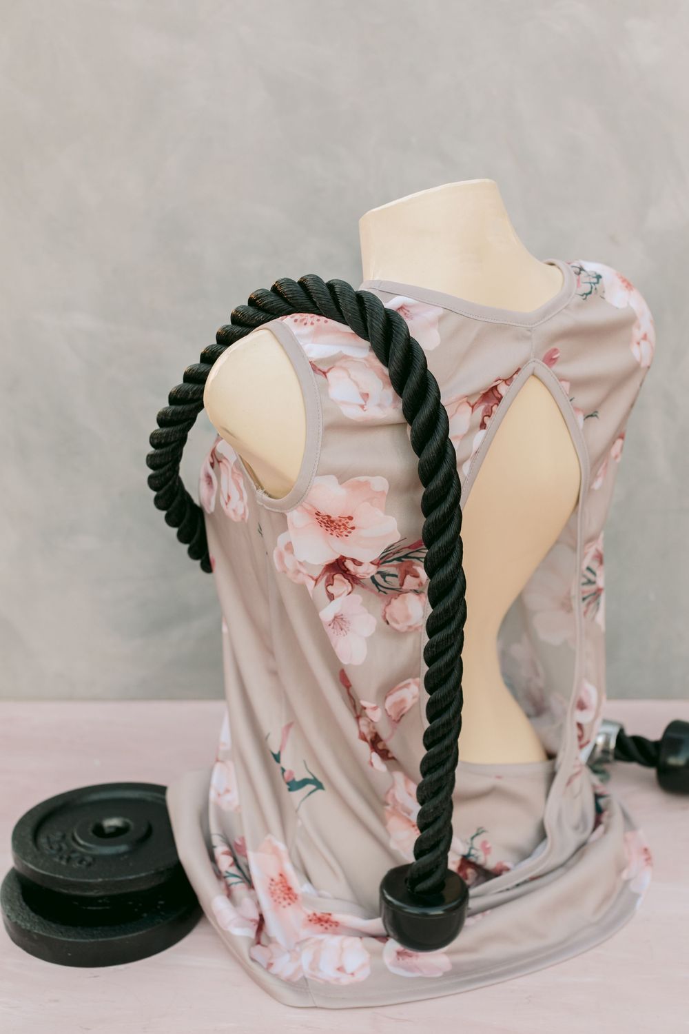A floral dress displayed on a mannequin torso with a rope cable attachment and weight plate nearby.