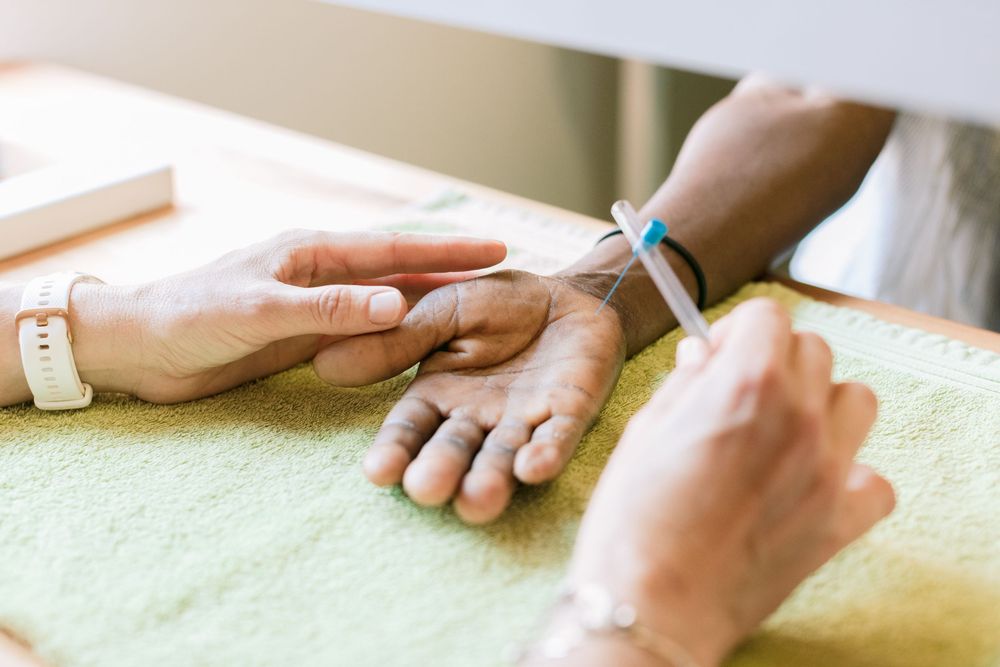 Healthcare professional inserting an IV line into a patient's hand on a green towel.