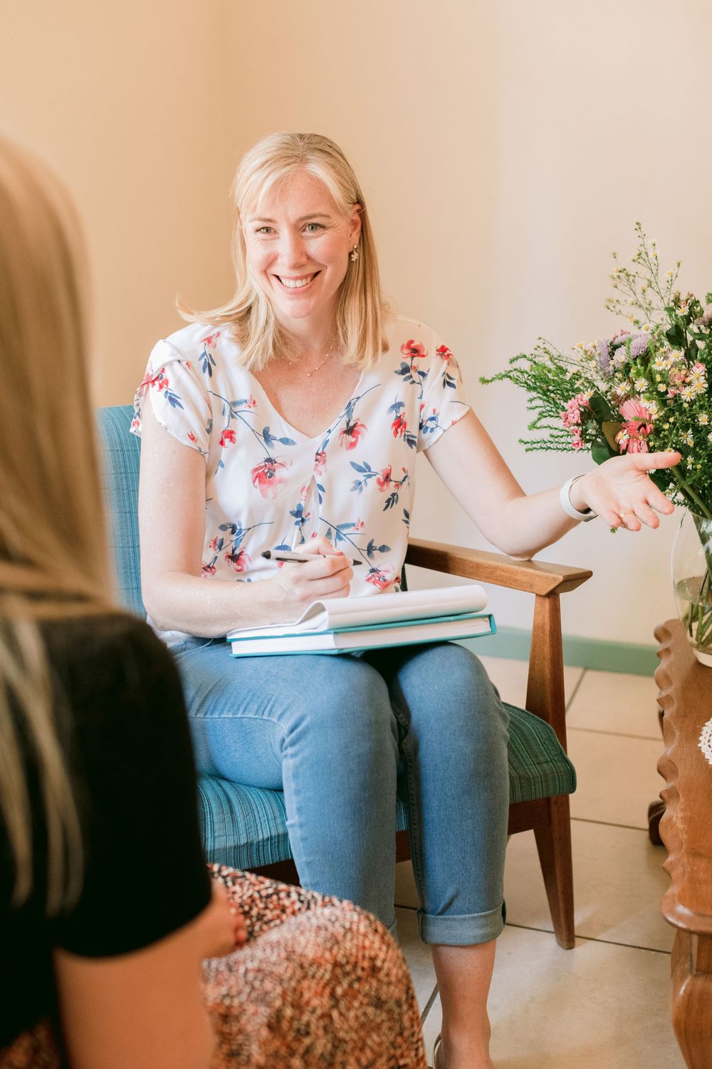 Smiling blonde woman in floral top taking notes during a counseling session.
