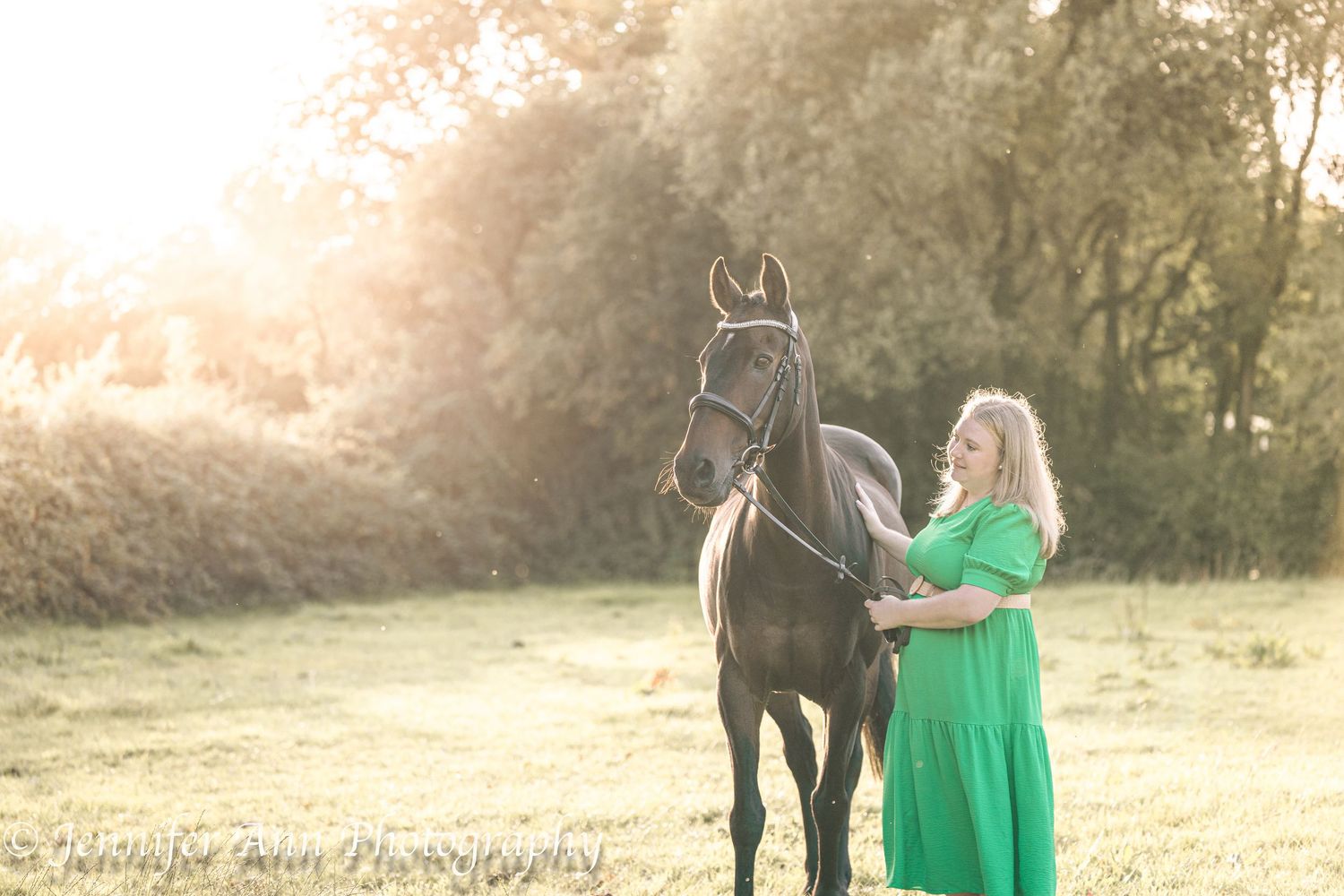 A couple in formal attire walks through a sunlit meadow with their horse during a romantic outdoor photoshoot.