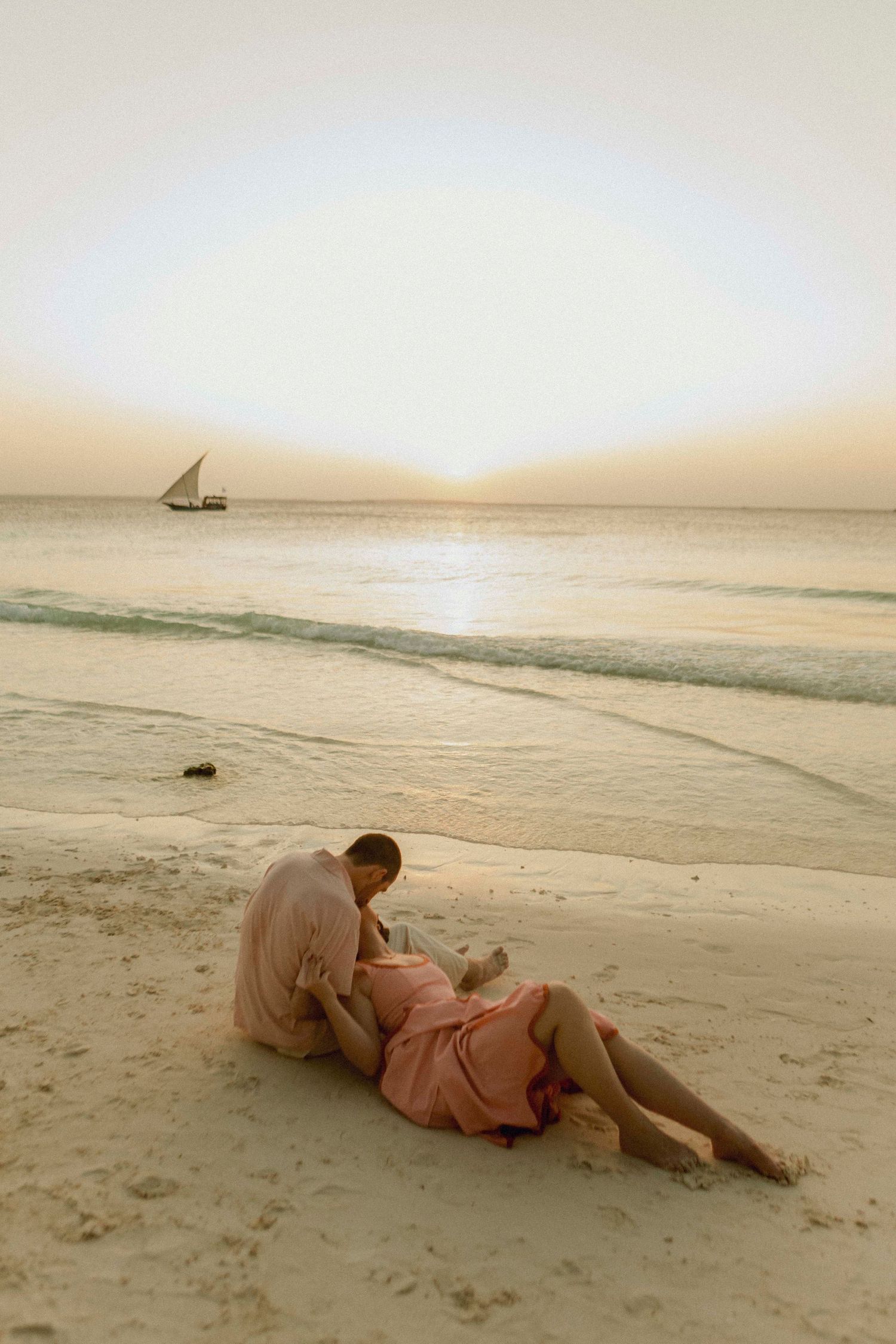 Couple sitting on beach rocks with ocean waves at Nungwi