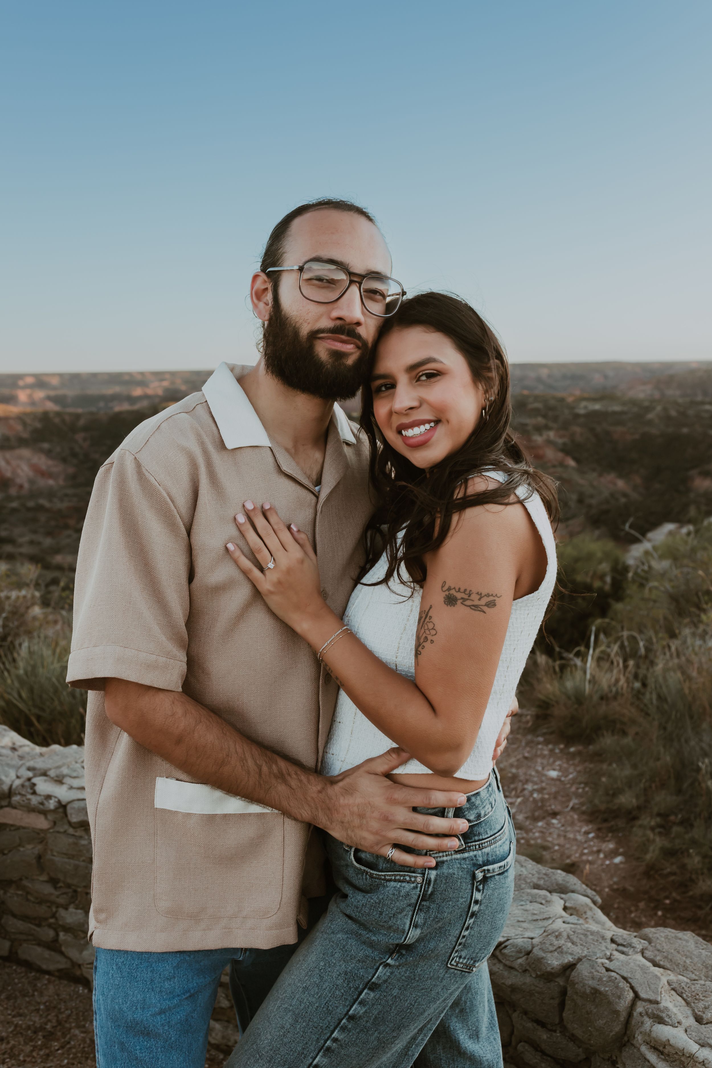 Smiling couple embracing at scenic canyon overlook during golden hour.