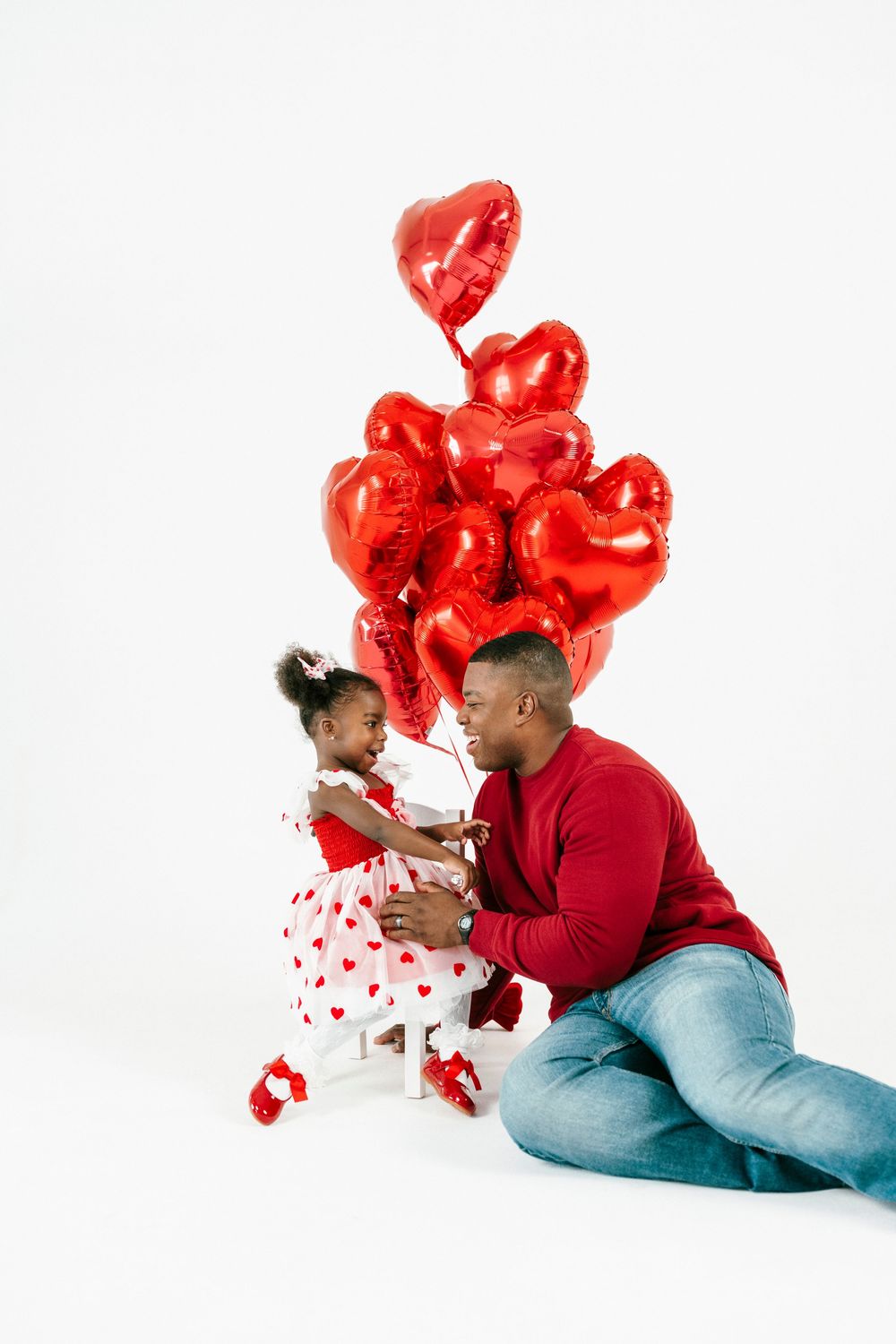 A couple lies on white backdrop with red heart-shaped balloons creating a romantic Valentine's Day portrait series.