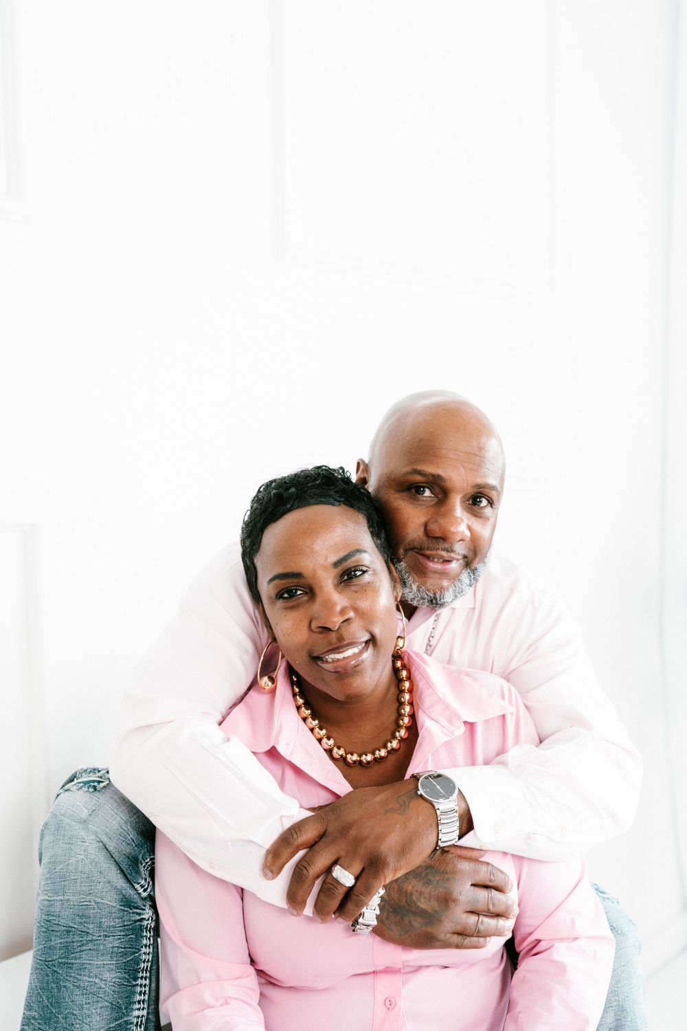 Couple in matching pink and denim outfits pose together against white background for intimate portrait session.