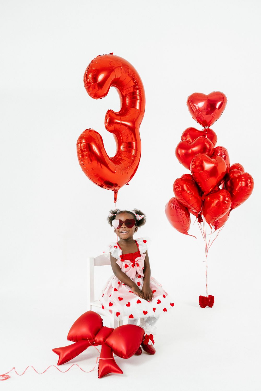 Red balloon number three and heart balloons create a festive Valentine's Day themed photo shoot setup.
