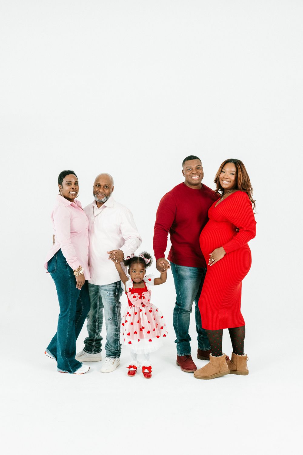 A family of five poses together against a white backdrop wearing coordinated red, pink and white outfits.