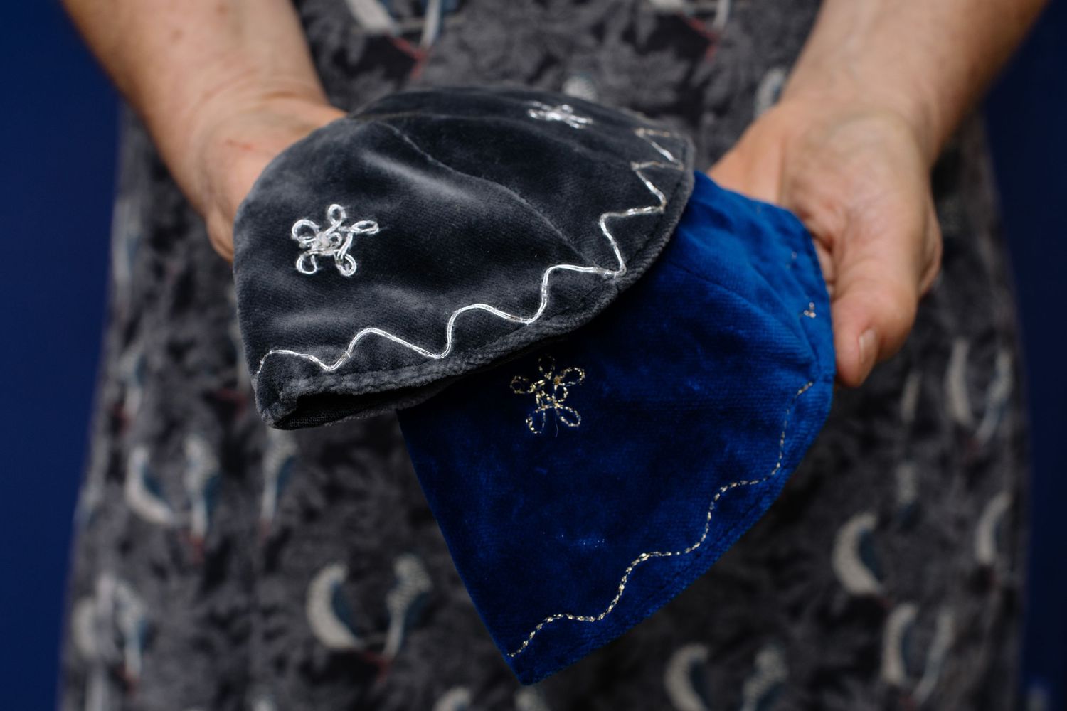 Hands holding vintage black and white portrait photographs against a dark blue background with yellow floral pattern.