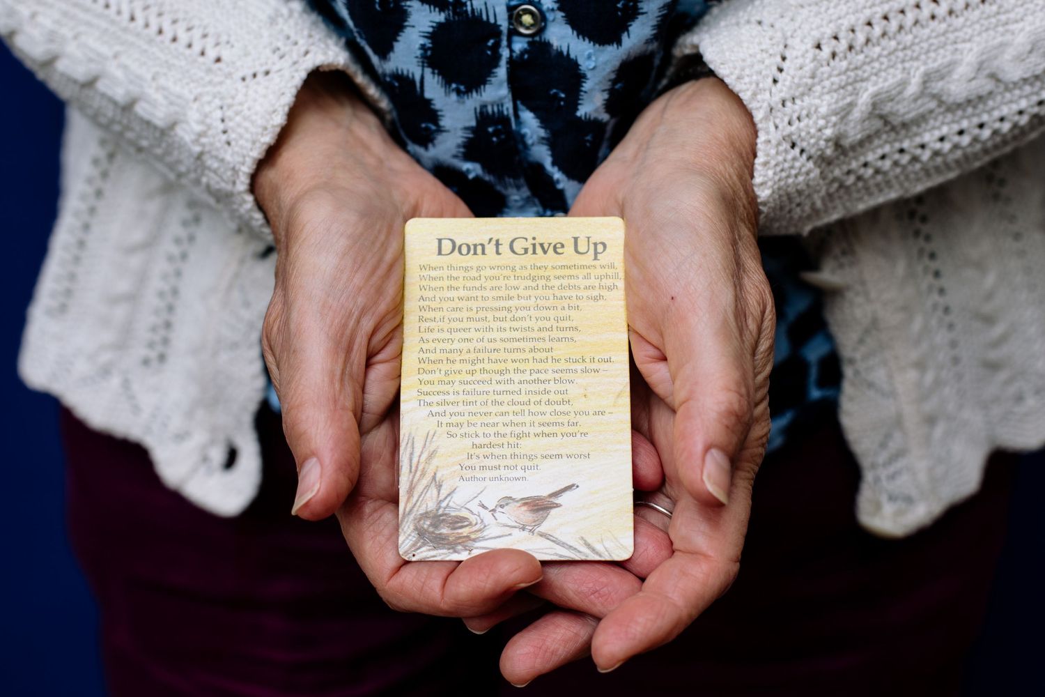 Hands holding vintage black and white portrait photographs against a dark blue background with yellow floral pattern.