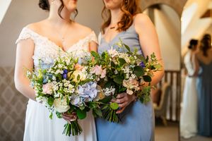 Close-up of bride and bridesmaid holding lush bouquets with hydrangeas, roses and greenery on wedding day.