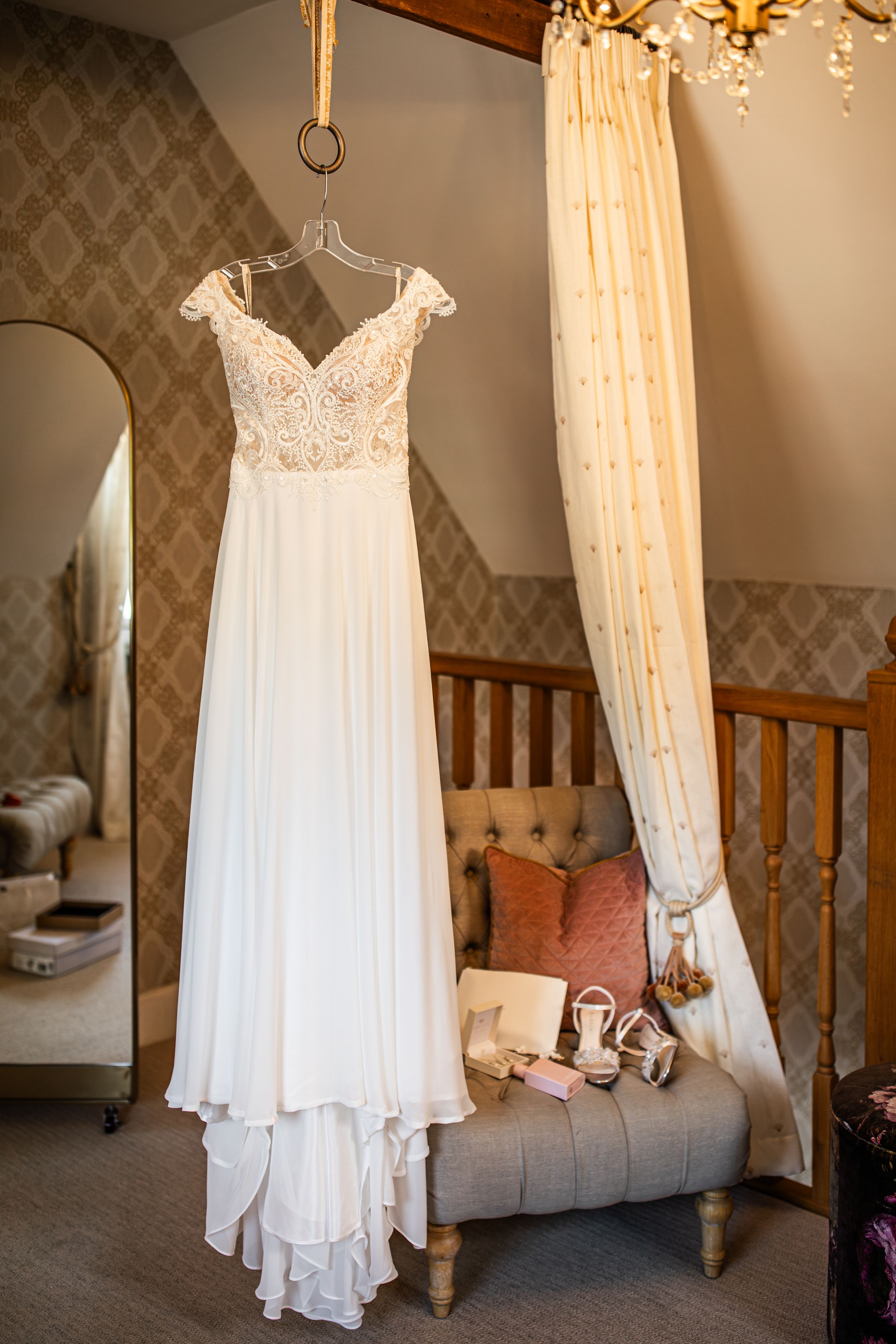 Elegant lace wedding dress hanging near a four-poster bed with bridal shoes and accessories below.