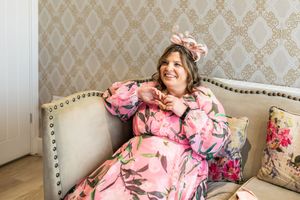 Joyful woman in pink floral dress and matching bow headband relaxing on elegant sofa smiling.