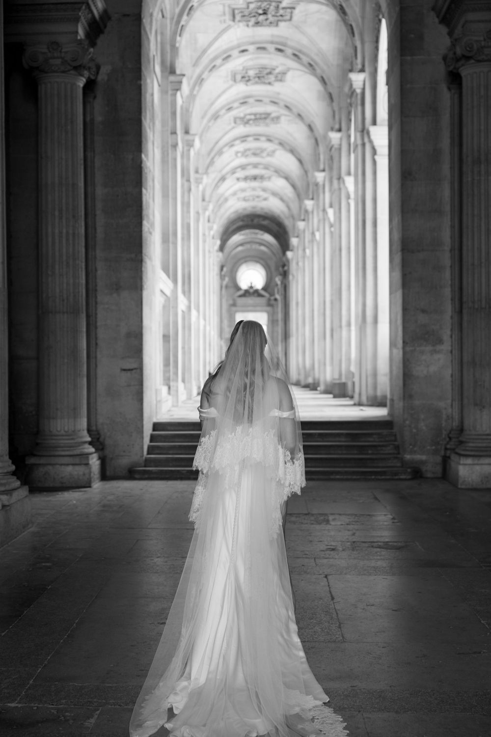 Ethereal bridal portrait in a grand columned hallway with dramatic black and white lighting.
