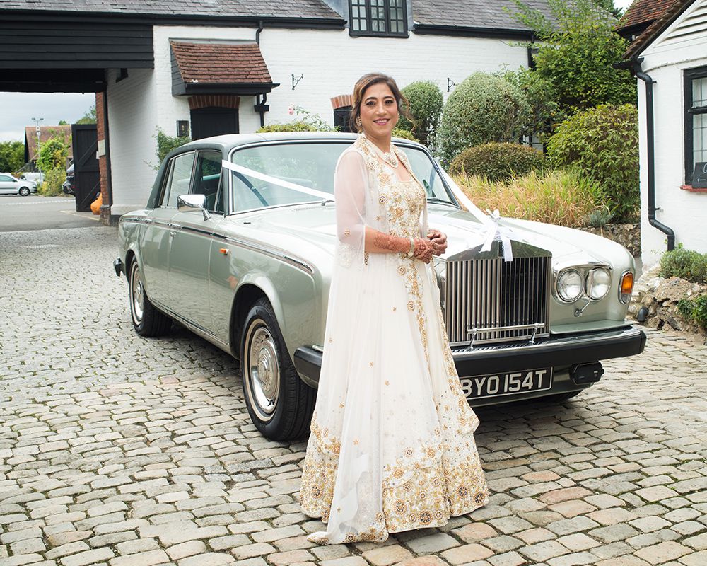 A bride in a white dress poses next to a car, featured in wedding photography by Abigail's Studio in High Wycombe.