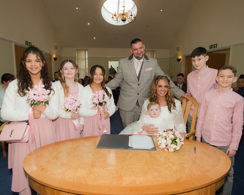 A group of smiling people poses together with a baby, captured during a wedding in High Wycombe by Abigail's Studio.