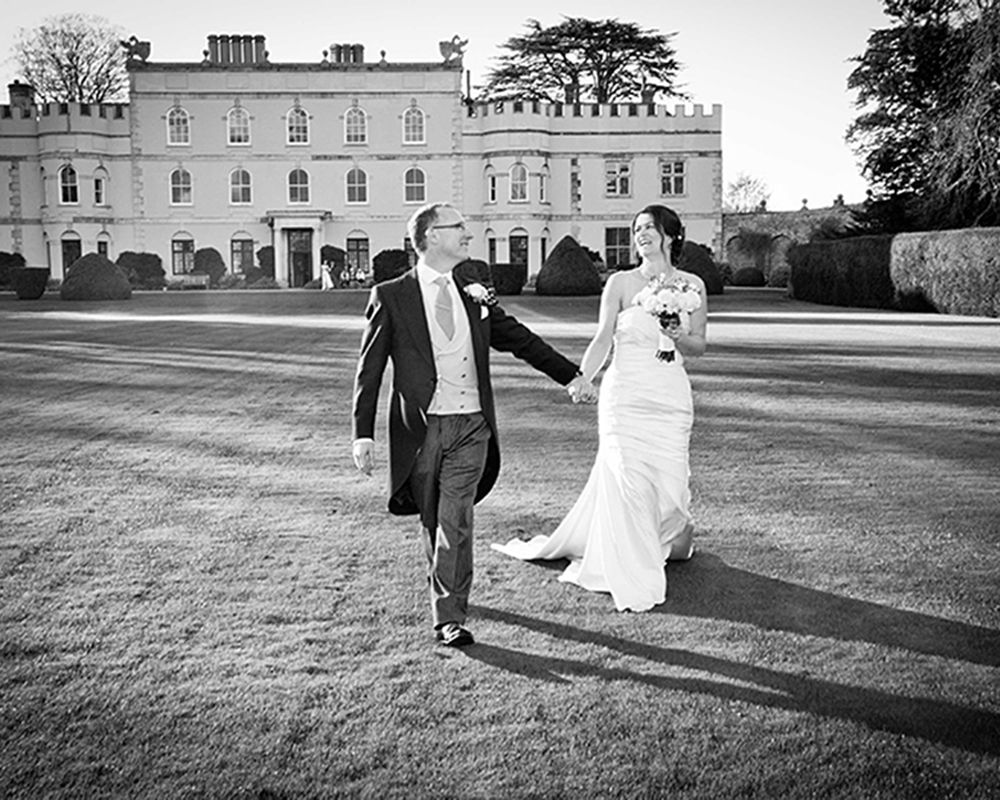A bride and groom stroll together in front of a grand mansion, captured by Abigail's Studio in High Wycombe.