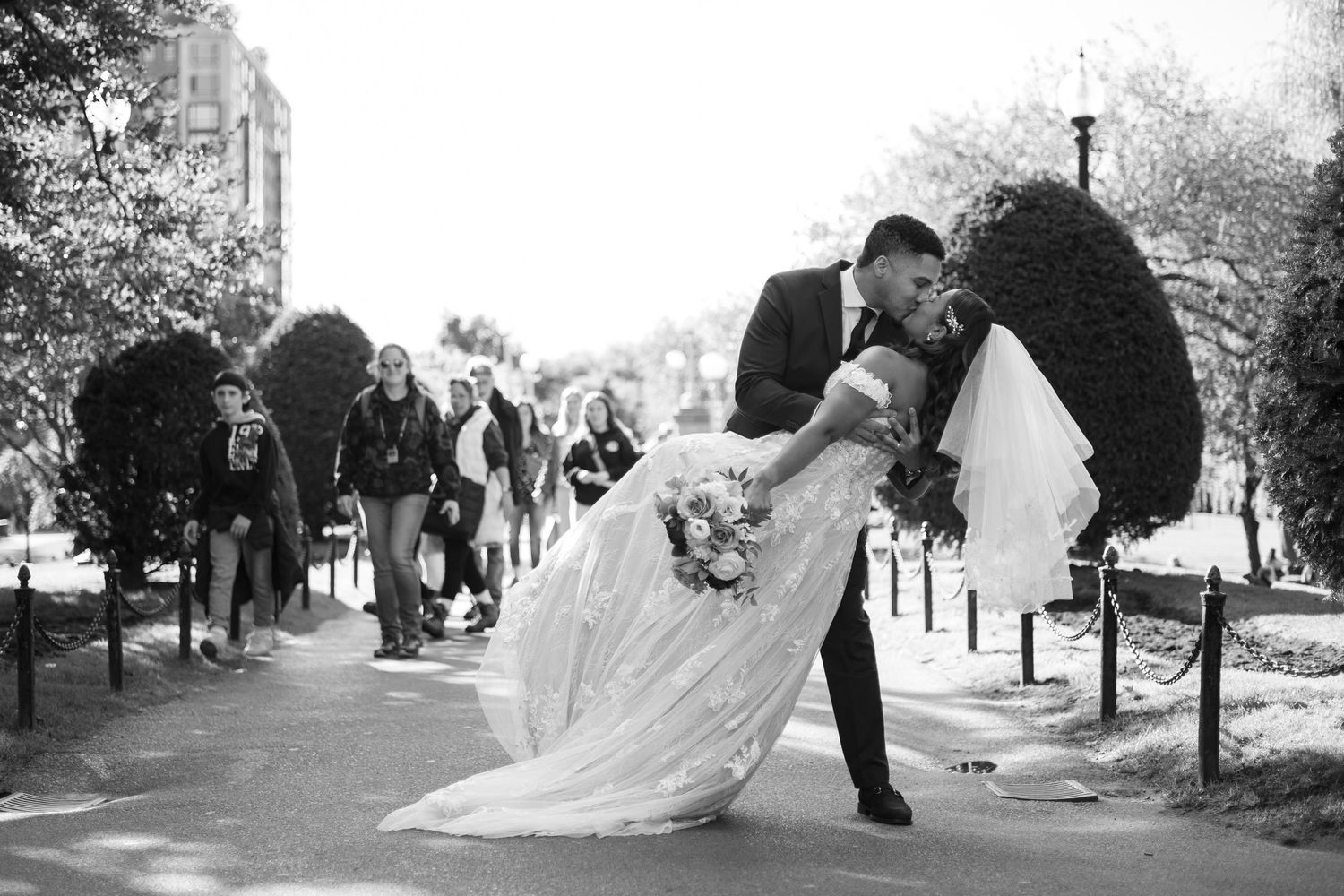 A black and white photo showing a wedding couple dipping in the Boston Public Gardens on their wedding day.