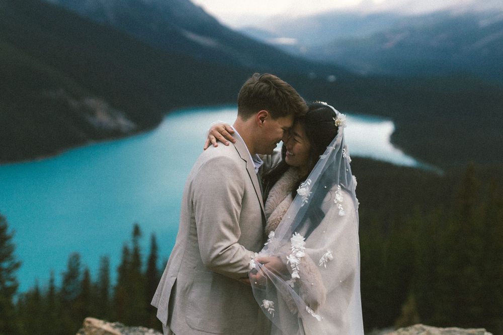 bride and groom laugh with their noses pressed together surrounded by as turquoise mountain lake in Banff
