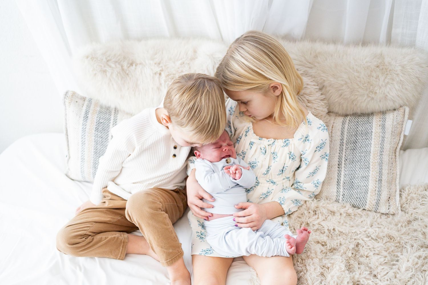 A mother and daughter sit together on a white couch in a bright, cozy living room.
