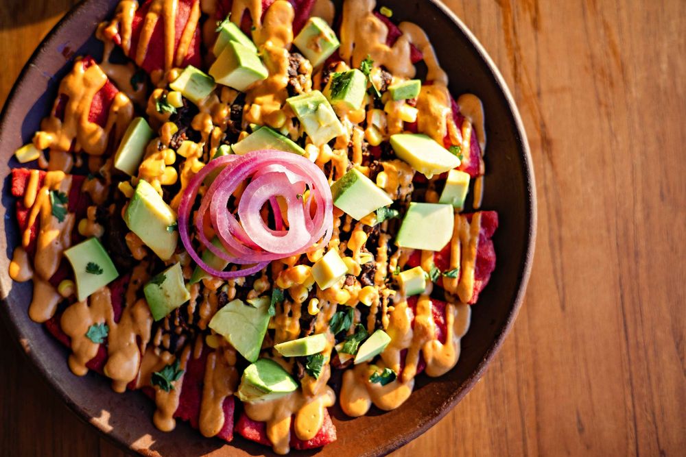 Mexican-style loaded nachos topped with avocado, red onions and cheese in a cast iron skillet.