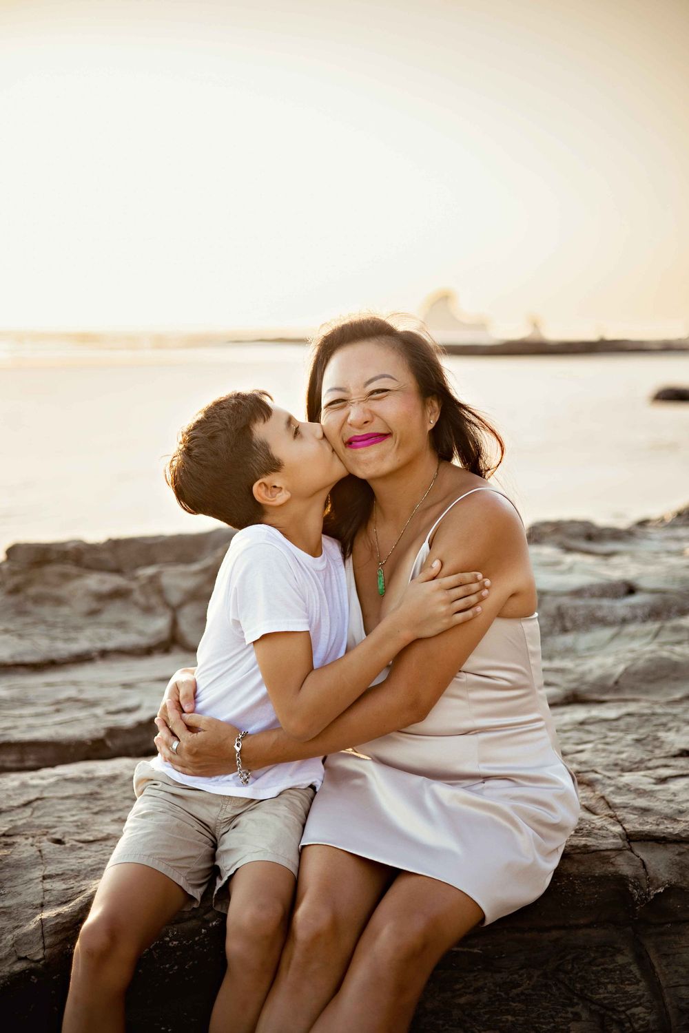 A tender moment between mother and child sitting on coastal rocks at sunset.