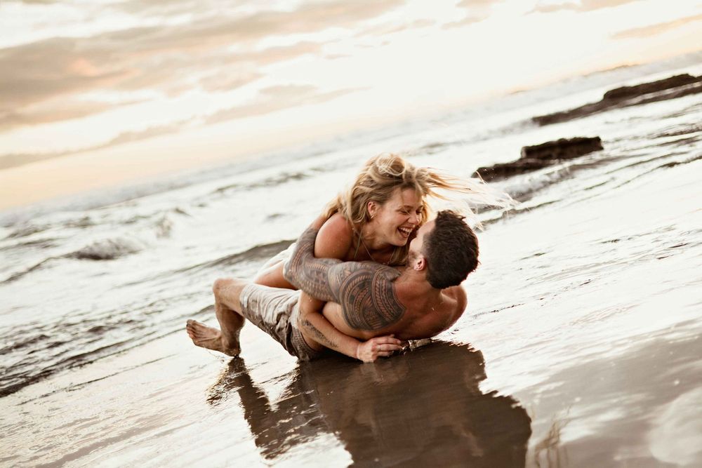 Person lying on wet sand at the beach during sunset with dramatic lighting.