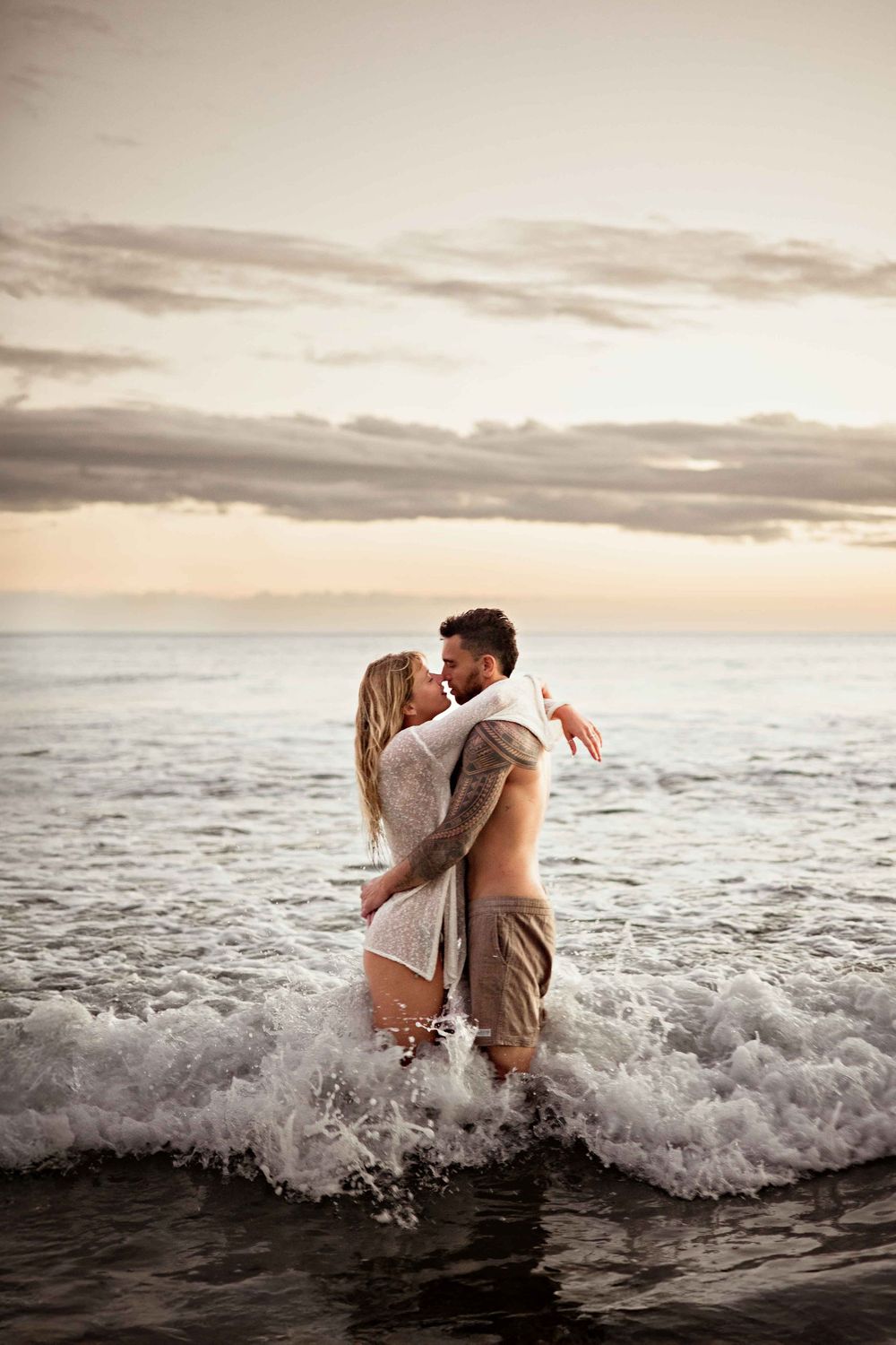 A romantic couple embraces in the ocean waves at sunset creating a dreamy silhouette against the seascape.
