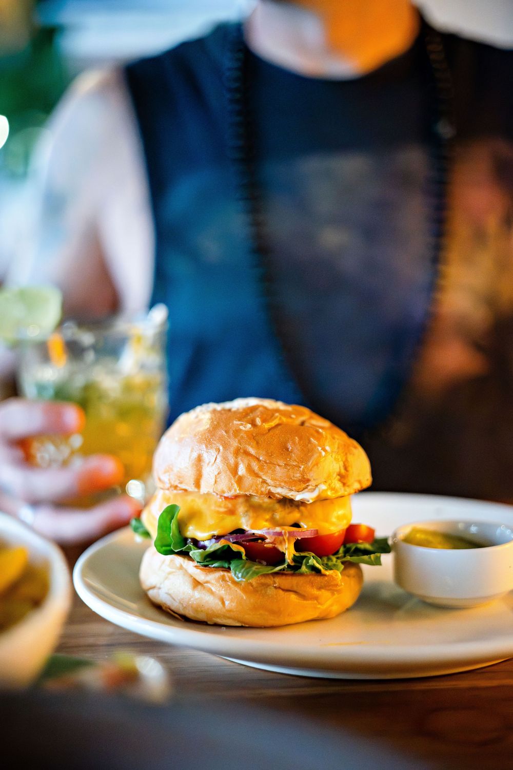 Juicy hamburger with fresh lettuce, tomato and cheese served on a white plate in restaurant lighting.