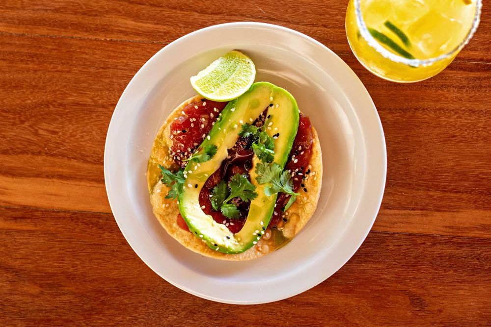 Overhead view of six tacos on small white plates arranged in a row on a wooden surface.