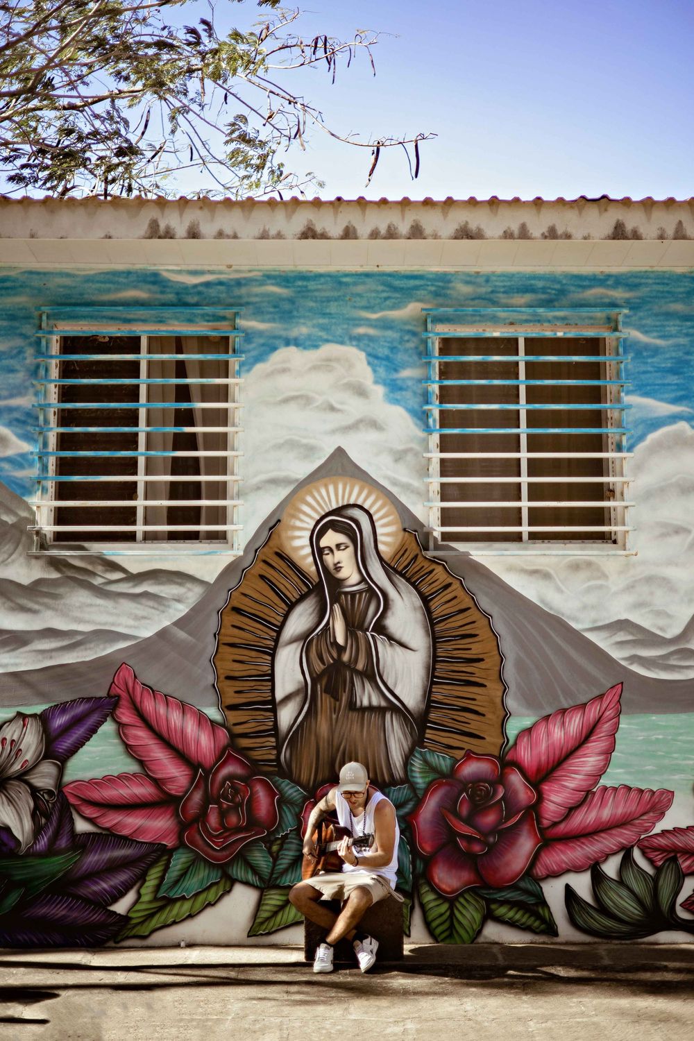 A sequence of street art murals showing a religious figure with roses against a cloudy sky background.