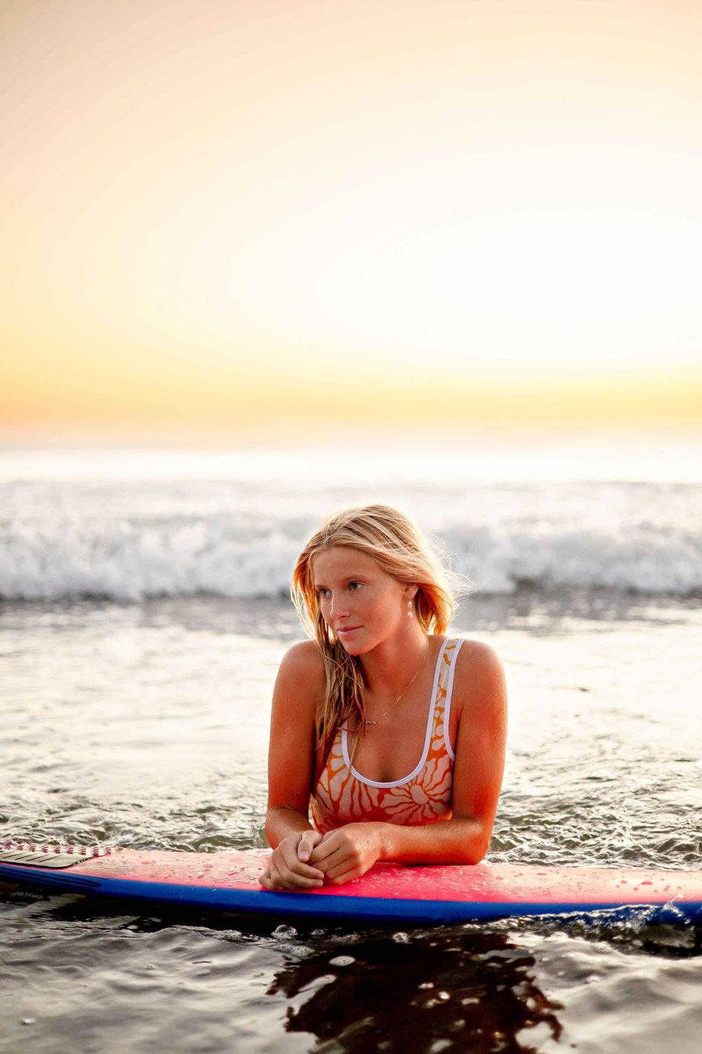 Surfer lying on surfboard at sunset with golden light reflecting on ocean waves.