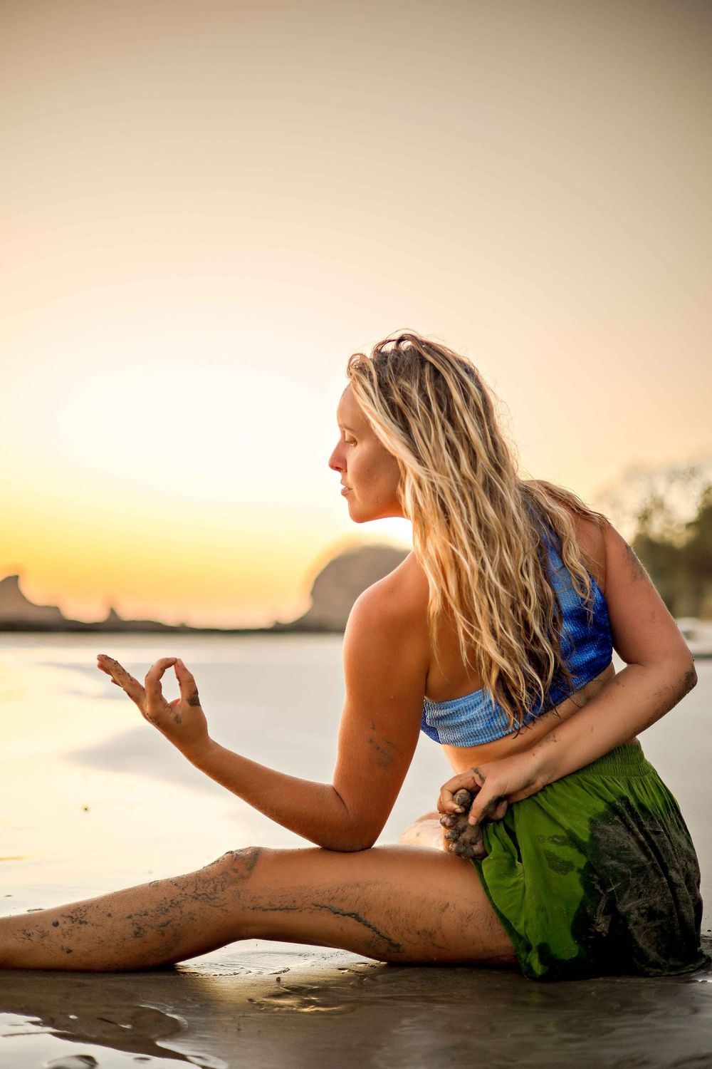 Person in blue and green swimwear posing on wet sand during golden hour at beach.