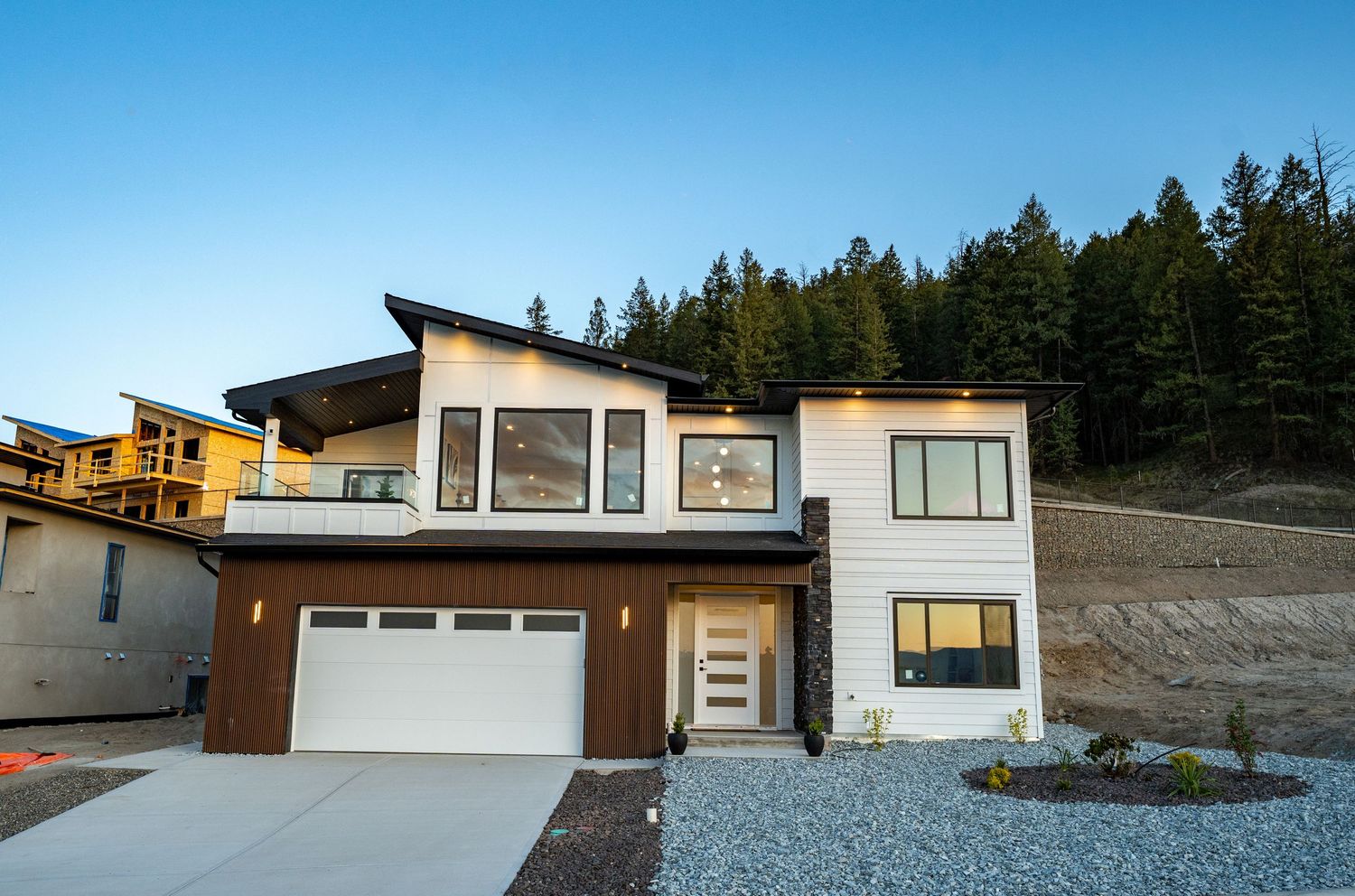 Modern mountain home exterior features clean lines, large windows, and natural wood accents against a scenic forest backdrop.